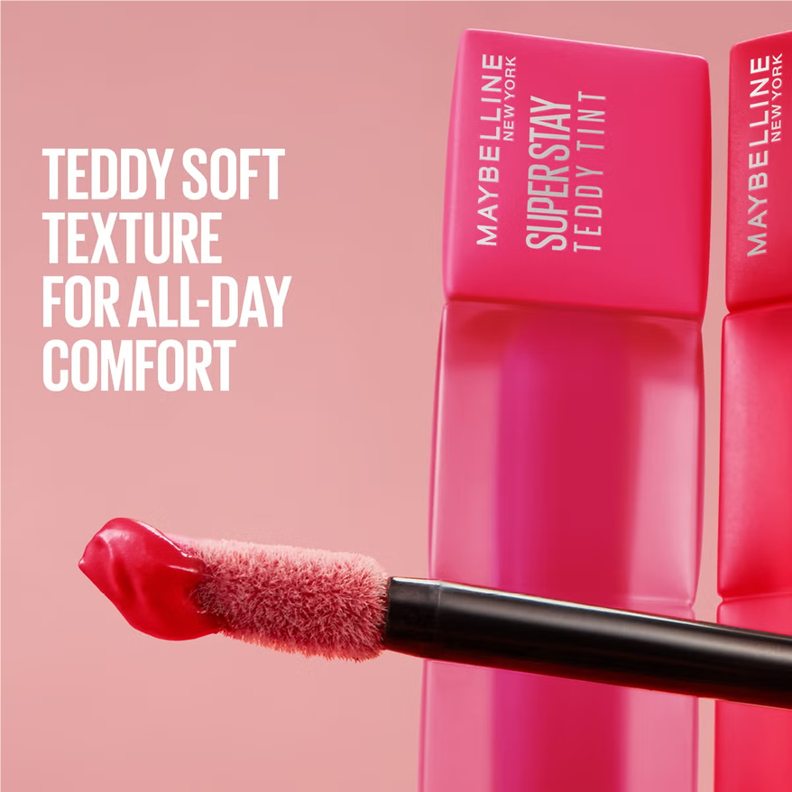 A creative stack of Maybelline SuperStay Teddy Tint Liquid Lip Tints arranged like building blocks against a pink background, showcasing the square matte-finish bottles in a range of nude, coral, and berry shades with bold white branding on the caps.