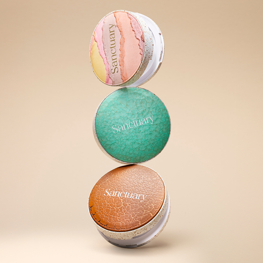 HCP Sanctuary trend packaging – trio of Radii Round Pressed Powder compacts with textured top-plates in earthy brown, speckled mint, and marbled pastel tones on a warm beige background