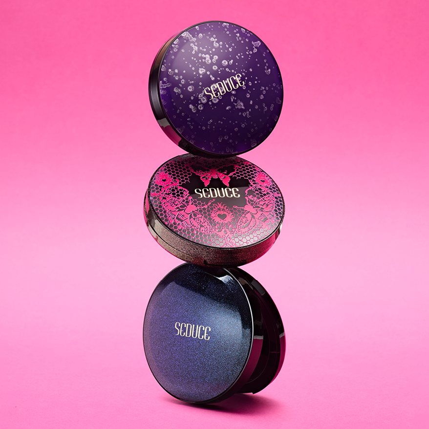HCP Seduce trend packaging – trio of Radii Round Pressed Powder compacts with dark, luxurious top-plates featuring lace, sparkle, and gradient effects on a pink satin background